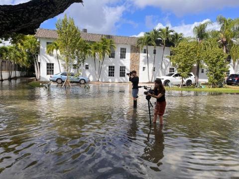 woman standing in flood waters with camera set up on tripod