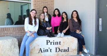 six students sit on a rock that says "Print Ain't Dead"
